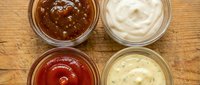 Four different condiment sauces in glass bowls on wooden background for cooking and food preparation.