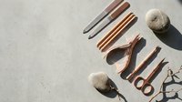 Rose gold manicure tools set with nail file, cuticle nipper, scissors, and pushers arranged on gray concrete surface with stones.