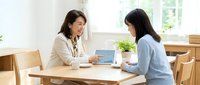 Two professional Asian women having business meeting discussion with laptop computer in bright modern office space for corporate consultation and teamwork.