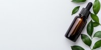Brown glass dropper bottle with green leaves on white background, minimal spa composition for natural cosmetics, aromatherapy and wellness products.