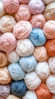 Soft pastel yarn balls in pink, blue, and peach tones arranged in gentle composition, showcasing natural cotton thread texture for knitting and crochet projects.