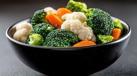 Fresh steamed vegetables in black bowl with broccoli, cauliflower and carrots on dark background, healthy vegetarian meal for clean eating and dieting.