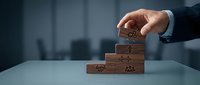 Businessman hand placing wooden blocks with teamwork icons in pyramid formation representing leadership hierarchy and organizational structure development.