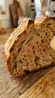 Sliced artisan raisin bread with golden crust and airy crumb structure on wooden surface in bakery kitchen setting for food photography and culinary content.