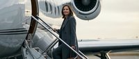 Professional businesswoman boarding private jet aircraft smiling confidently at airport during golden hour sunset for luxury travel and corporate success.