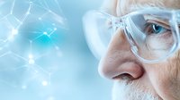 Senior Caucasian man in protective glasses observing molecular structure visualization against blue background, close-up view of scientific research concept.