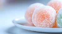 Colorful sugar-coated jelly candies on white plate with soft pastel background for sweet treats and confectionery marketing materials.
