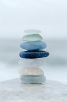 Stack of smooth sea glass stones in blue green white colors balanced on sandy beach for meditation wellness and mindfulness practices.