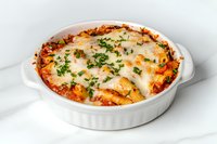 Baked pasta casserole with melted mozzarella cheese, marinara sauce and fresh herbs in white ceramic dish, homestyle Italian comfort food on light background.