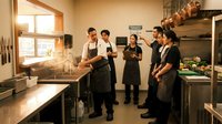 Professional culinary team meeting in modern commercial kitchen during food preparation and training session.