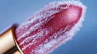 Frozen lipstick covered in ice crystals against blue background, extreme macro photography showing detailed frost formation on cosmetic product surface.