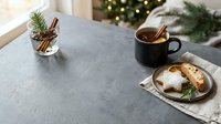 Cozy holiday table setting with warm beverage in black mug, fresh pastries dusted with powdered sugar, and festive greenery decorations for seasonal celebrations and winter gatherings.