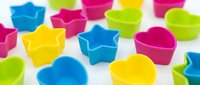 Colorful silicone baking molds in star and heart shapes scattered on white background. Bright kitchen accessories for cupcakes and desserts preparation.