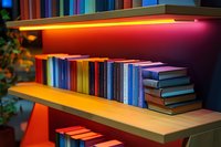 Colorful books arranged on wooden shelves with dramatic LED lighting creating warm ambiance, multicolored spines in rainbow order for modern library or bookstore display.