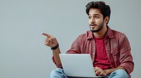 Young South Asian male professional in casual attire working on laptop while gesturing and looking away, expressing confidence and engagement in remote work setting.