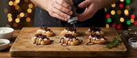 Hands decorating chocolate desserts on wooden board with festive bokeh lights creating warm holiday baking atmosphere for seasonal celebrations.