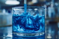 Vibrant blue liquid swirling in clear glass creating mesmerizing abstract patterns as it mixes with water, captured in macro photography against blurred background.