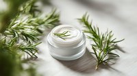 Fresh rosemary-infused face cream in white jar on wooden surface, surrounded by aromatic herb sprigs for natural skincare products.