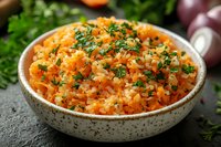 Fluffy rice pilaf with diced carrots and fresh chopped parsley in ceramic bowl. Traditional homestyle side dish garnished with herbs on dark background.