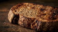 Freshly baked whole grain bread loaf with crispy crust on rustic wooden surface, suitable for bakery, food, and culinary design projects.