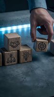 Businessman hand placing wooden cube with gear icon among business symbol blocks representing strategy planning and teamwork concepts.