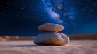 Balanced stones on sandy beach against starry night sky with vibrant Milky Way galaxy. Zen meditation and mindfulness concept for spiritual wellness.