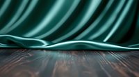 Luxurious dark green silk fabric draped over wooden surface creates elegant backdrop with soft folds and dramatic lighting for product photography and presentations.