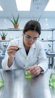 Female scientist of East Asian descent conducting chemical analysis in modern laboratory, holding dropper over liquid sample. Research and development.