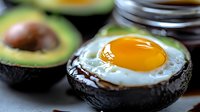 Fresh sunny side up egg served in ripe avocado half with bright yellow yolk, close up view on dark background. Healthy keto breakfast preparation.