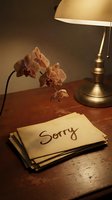 Vintage sorry note on aged paper beside dried orchid and brass lamp on wooden desk, evoking apology, regret, and heartfelt emotion.