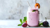 Fresh pink smoothie with plums and cherries in mason jar, garnished with mint leaves and fruit on light background, healthy breakfast drink.