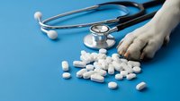 Medical stethoscope with scattered white pills and tablets on blue background. Healthcare, pharmacy and medicine concept for clinical treatment.