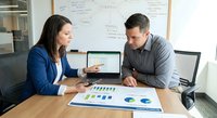 Business professionals analyzing financial data and charts in modern office meeting room with laptop and documents on conference table.
