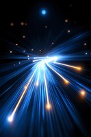 Dynamic blue light rays burst forward with glowing orange particles against dark background, creating dramatic perspective and sense of high-speed motion and energy flow.
