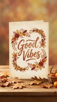 Autumn greeting card with Good Vibes text surrounded by fall leaves wreath on wooden table with warm bokeh background for seasonal celebrations.
