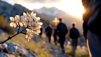 Cherry blossom branch in focus with silhouettes of pilgrims walking towards mountain cross at sunset, spiritual spring landscape composition.