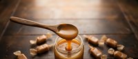 Wooden spoon drizzling golden honey into glass jar on rustic wooden table with scattered walnuts creating warm cozy kitchen atmosphere for cooking baking.