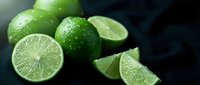 Fresh green limes with water droplets, whole and sliced showing juicy citrus flesh on dark background for cooking, beverages and healthy nutrition concepts.