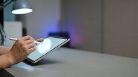 Close-up of male hand holding tablet device with glowing screen on desk under lamp in modern office workspace for technology and business concepts.