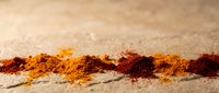 Spice powder line arranged on sandy surface, featuring turmeric and paprika in warm tones for culinary and cooking content.