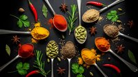 Colorful spices and herbs arranged on wooden spoons against dark background. Culinary ingredients including turmeric, paprika, cardamom for cooking and seasoning.