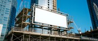 Blank white billboard on scaffolding at urban construction site with modern skyscrapers and blue sky, mockup for outdoor advertising.