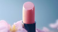 Pink lipstick close-up macro shot against soft blurred background with delicate flower petals, showcasing cosmetic product detail and texture.