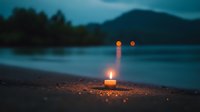 Glowing candle on sandy beach at dusk with blurred water and forest silhouettes in background, creating atmospheric moody scene with bokeh light reflections.