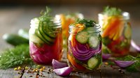 Fresh pickled vegetables in glass jars with cucumber, red onion, carrot and dill. Homemade fermented food for healthy gut microbiome and immunity boost.