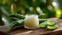 Natural aloe vera gel in glass jar with fresh cut leaves and slices on wooden surface against blurred green garden background. Organic skincare concept.