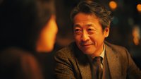 Mature Asian businessman smiling warmly in elegant restaurant setting with soft candlelight creating intimate atmosphere for dining and conversation.