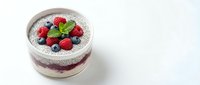 Chia seed pudding layered with yogurt and fresh raspberries, blueberries, topped with mint leaf in glass cup on white background.