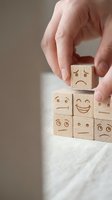 Hand arranging wooden blocks with engraved emoji faces showing various emotions, from happy to sad, on a light surface.