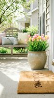 Sunny front porch with pink and yellow tulips in a ceramic pot, welcome mat, and wooden bench with pastel pillows in spring.